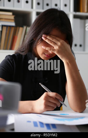 Stanco ed esausto donna guarda a documenti appoggiando la sua testa con le mani Foto Stock