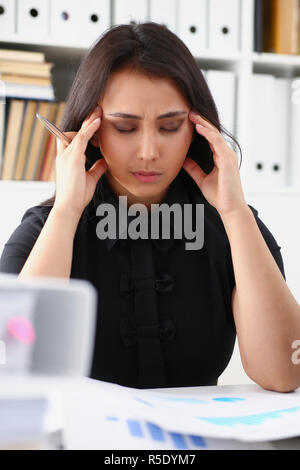 Stanco ed esausto donna guarda a documenti appoggiando la sua testa con le mani Foto Stock