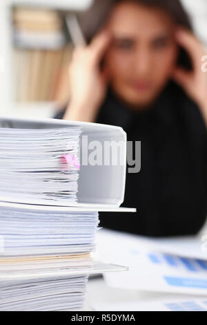 Stanco ed esausto donna guarda a documenti appoggiando la sua testa con le mani Foto Stock