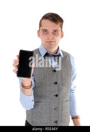 Un bel giovane uomo in piedi in un giubbotto grigio, maglietta blu e un papillon, tenendo in mano il suo telefono cellulare, isolato per sfondo bianco Foto Stock