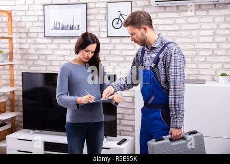 Tecnico maschio assistere giovane donna nella fattura di firma a casa Foto Stock