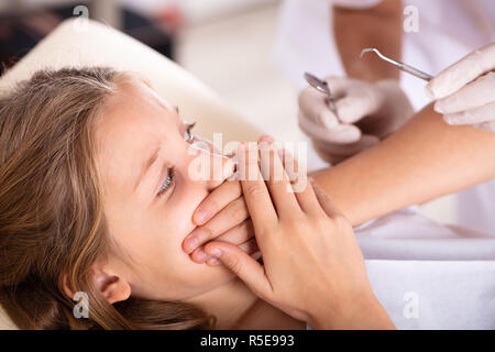 Spaventata ragazza che copre la bocca con le mani mentre attraversa il trattamento dentale in clinica Foto Stock