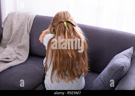 Vista posteriore di una ragazza triste seduto sul divano di casa Foto Stock