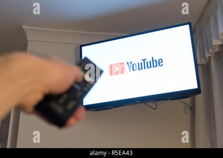 Un uomo punti a controllo remoto a una televisione intelligente visualizzando l'app YouTube in una camera da letto a casa nel Regno Unito. Novembre 2018. Foto Stock