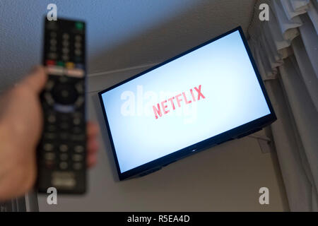 Un uomo punti a controllo remoto a una televisione intelligente visualizzando il Netflix app in una camera da letto a casa nel Regno Unito. Novembre 2018. Foto Stock