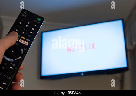 Un uomo punti a controllo remoto a una televisione intelligente visualizzando il Netflix app in una camera da letto a casa nel Regno Unito. Novembre 2018. Foto Stock