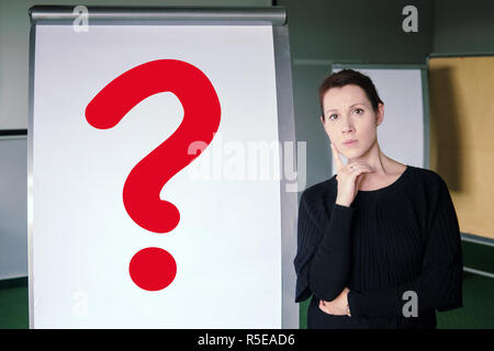 Brunette donna in piedi accanto alla lavagna a fogli mobili con il punto interrogativo rosso Foto Stock