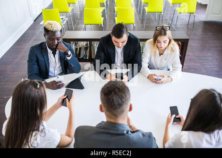 Ufficio di diverse persone che lavorano su telefoni cellulari, i dipendenti corporate holding smartphone alla riunione Foto Stock