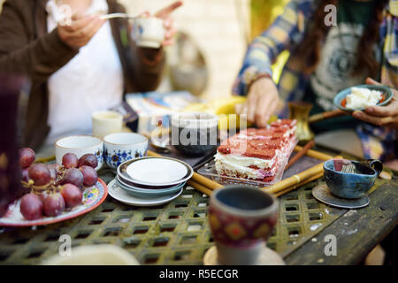 Bella tavola dessert con colorate tazze di ceramica, piattini, una deliziosa torta di carote e frutta. Mangiare dolci e dessert all'esterno. Foto Stock