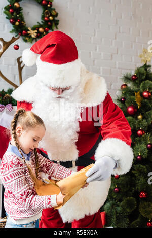 Santa Claus guardando il piccolo bambino con wishlist Foto Stock