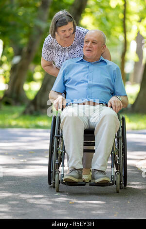 Senior donna spingendo il marito in carrozzella Foto Stock