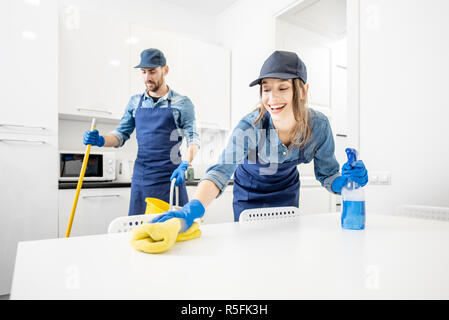 L uomo e la donna come pulitori professionali in un lavaggio uniforme pavimento e mobili di tergitura in cucina bianca. Il servizio di pulizia concept Foto Stock