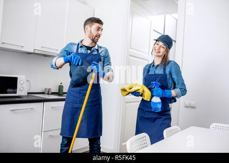 Ritratto di un giovane stanco in piedi come pulitori professionali in uniforme durante la pausa in cucina Foto Stock