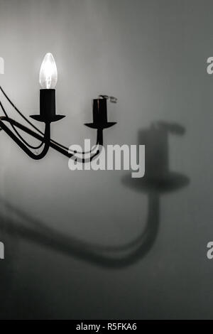 La lampadina rotta in un lampadario a bracci di montaggio della luce, getta un' ombra sul muro Foto Stock
