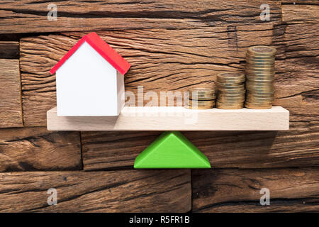 Monete impilate e modello di casa di equilibratura su altalena Foto Stock