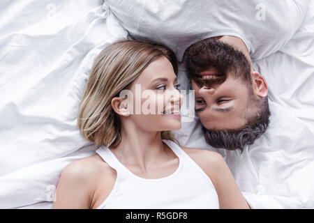 Coppia giovane in amore giacente testa a testa e cercando di ogni altro su coltre bianca Foto Stock