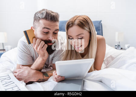 Sorridente coppia giacendo in letto e facendo shopping online Foto Stock