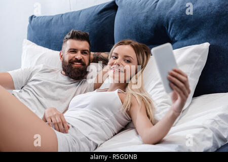 Gioiosa giovane in posa di letto e tenendo selfie in mattinata Foto Stock