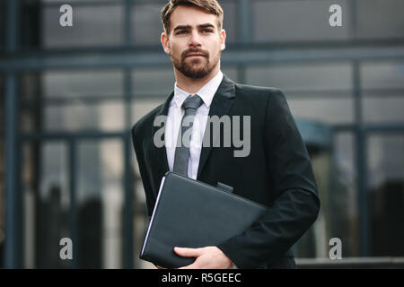 Ritratto di bello imprenditore con una cartella passeggiate all'aperto. Uomo in businesswear tenendo un file e guardando lontano. Foto Stock