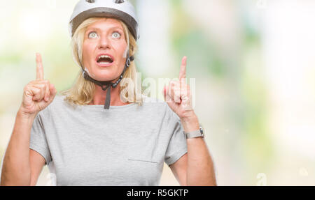 La mezza età caucasian ciclista donna che indossa il casco di sicurezza su sfondo isolato meravigliato e sorpreso cercando e dispositivo di puntamento con le dita e sollevato Foto Stock