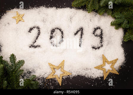 2019 scritto nella neve su sfondo nero decorato con rami verdi e Golden Stars Foto Stock