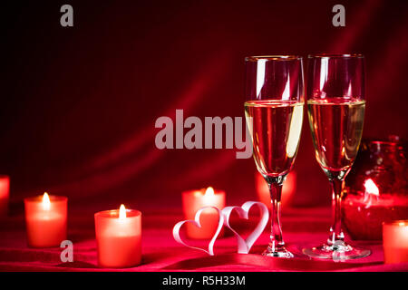 Il giorno di San Valentino festa, bicchieri di champagne, candele, rose e cuori su seta rossa Foto Stock