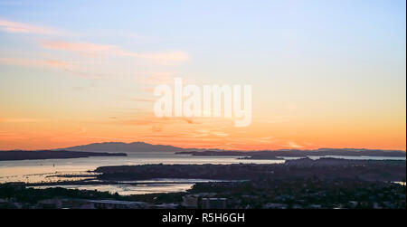 Albe su Auckland dalla sommità del monte Eden attraverso silhoutee città e il porto di Rangitoto Isola sull orizzonte. Foto Stock