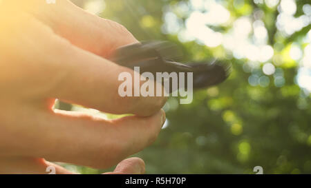 Giocando con il nero agitano: Spinner. Toy spinner in mano. Effetto sole Foto Stock