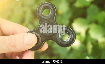 Giocando con il nero agitano: Spinner. Toy spinner in mano. Effetto sole Foto Stock