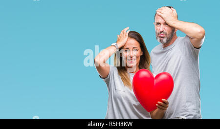 Medioevo ispanico casual giovane in amore azienda cuore rosso su sfondo isolato ha sottolineato con la mano sulla testa, sconvolto con vergogna e la sorpresa di fronte, Foto Stock