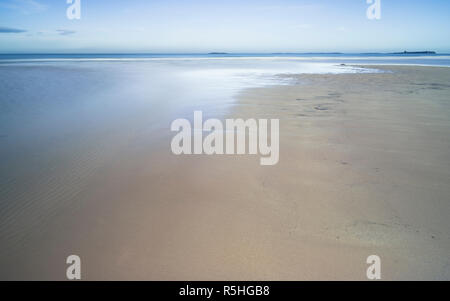 Un tranquillo scenario della spiaggia a Bamburgh, Northumberland, con sabbia e un ruscello che scorre verso il mare. Foto Stock