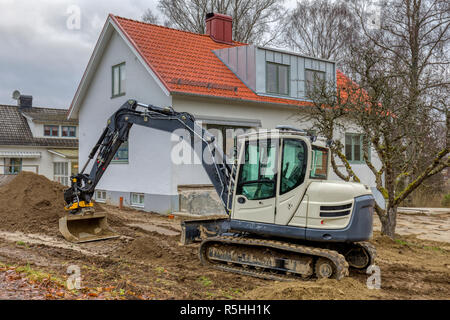 FLODA, Svezia - 21 novembre 2018: piccolo escavatore paesaggio facendo lavorare nel giardino di casa indipendente Foto Stock