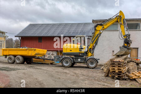 FLODA, Svezia - 21 novembre 2018: medie escavatore giallo con rimorchio in appoggio la benna sulla pila di palette di legno Foto Stock