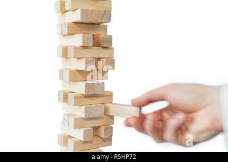 Mano d'uomo prendendo o mettere un blocco a un instabile e torre incompleta dei blocchi di legno. Concetto foto di pianificazione, tenendo conto dei rischi e la definizione di strategie. Foto Stock