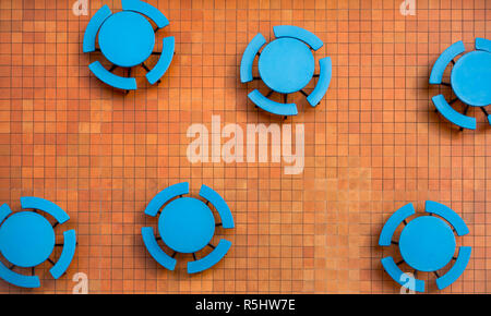 Piazza Orange patio tile e vuoto, blu rotondo di tabelle in un posto vacante food court offrono suggestivi contrasti di colore in un campione di forme geometriche pattern. Foto Stock