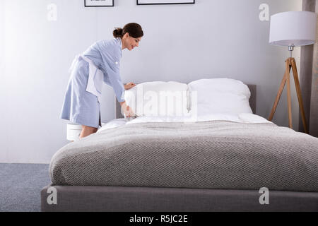 Donna sorridente governante rendendo letto in camera in hotel Foto Stock