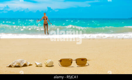 Occhiali da sole shell Coral Reef sulla spiaggia sabbiosa, barca in arrivo. Concetto di viaggio con sfondo sfocato Foto Stock