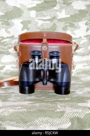 Vintage militare inglese a prisma di Porro colore nero binocolo con aperto brown una custodia in pelle con tracolla su sfondo di mimetizzazione vista frontale vicino Foto Stock