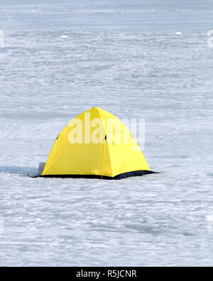 Pesca d'inverno. Fisherman tenda da giallo con fondo nero nella neve sul fiume congelato in giornata invernale closeup Foto Stock