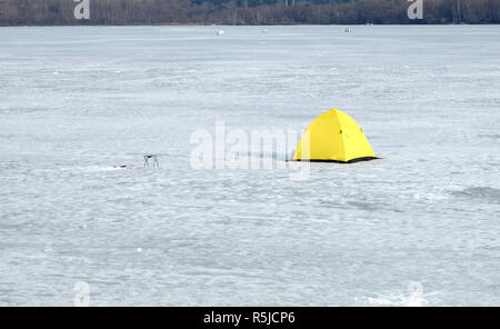 Pesca d'inverno. Fisherman tenda da giallo con fondo nero nella neve sul fiume congelato in giornata invernale closeup Foto Stock