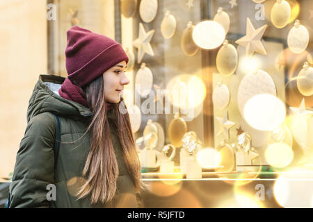 Una giovane bella donna o ragazza guarda la vetrina del negozio e sceglie un regalo di Natale. Foto Stock