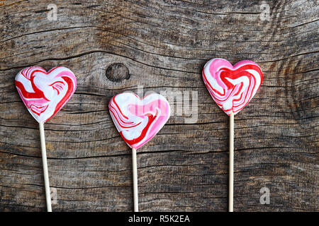 Tre bianco-rosso lecca lecca a forma di cuore su sfondo di legno Foto Stock