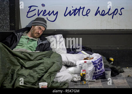 Il centro di Liverpool sleeping senzatetto di accattonaggio uomo con il disordine intorno a lui come egli dorme, ogni piccolo aiuta a tesco slogan Foto Stock