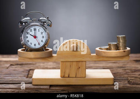 Orologio e monete in equilibrio su legno scala di pesatura Foto Stock