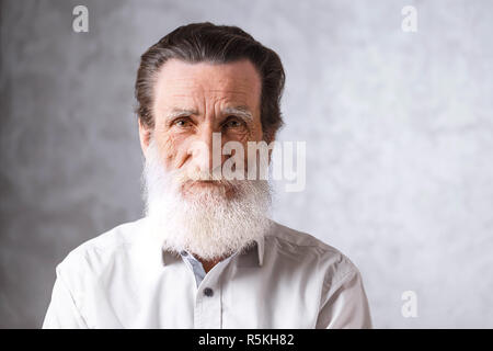 Ritratto di senior contemporaneo uomo barbuto con rughe in maglia bianca in piedi su uno sfondo grigio, tecnologia moderna, il concetto di comunicazione Foto Stock