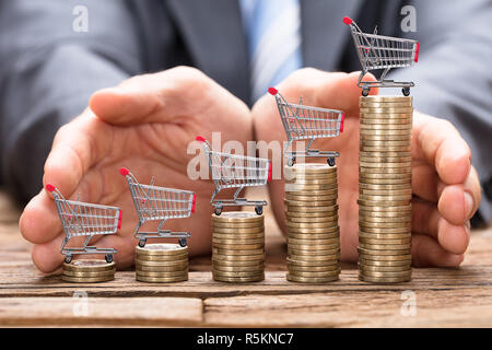 Imprenditore proteggendo i carrelli della spesa sulle monete impilate Foto Stock