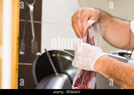 Un maschio di imballaggio a mano fino a fette di prosciutto crudo per essere venduto. Foto Stock