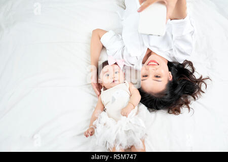 Una donna con un bambino facendo un selfie sdraiato sul pavimento in legno Foto Stock