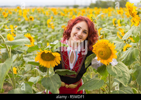 Ragazza in un tradizionale abito bulgaro sentirsi felice in un campo di girasoli Foto Stock