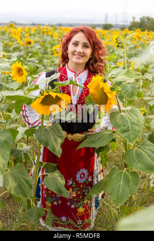 Ragazza in un tradizionale abito bulgaro sentirsi felice in un campo di girasoli Foto Stock